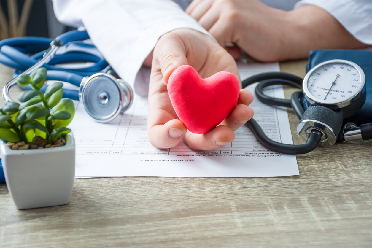 A doctor holding a red heart with a stethoscope, symbolizing care and medical expertise.