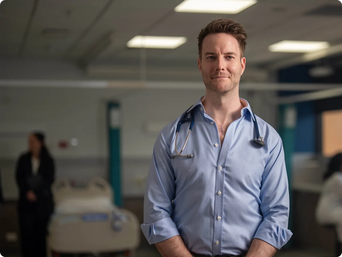 Dr Jeff Leicester standing in a hospital looking at the camera while having a stethoscope around his neck