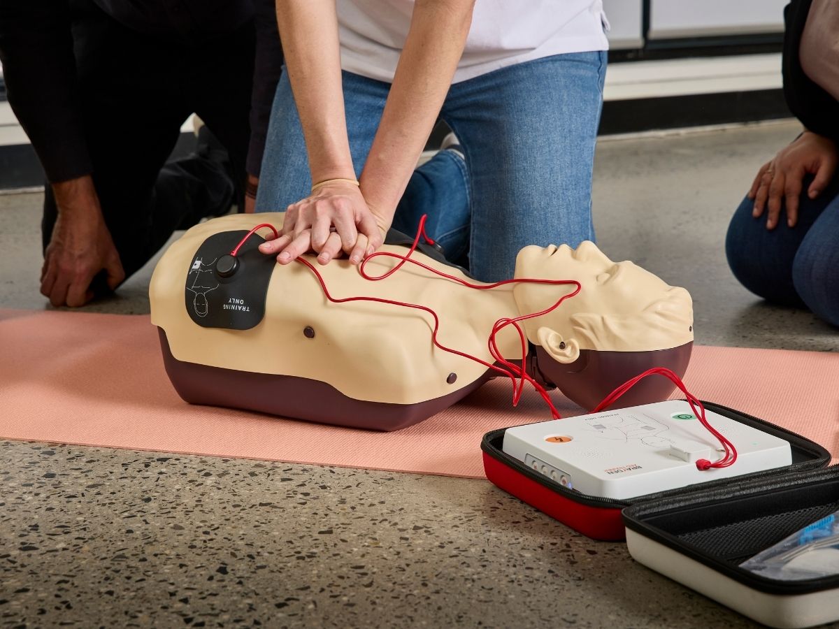 A woman doing compressions on a mannequin that has AED pad applied
