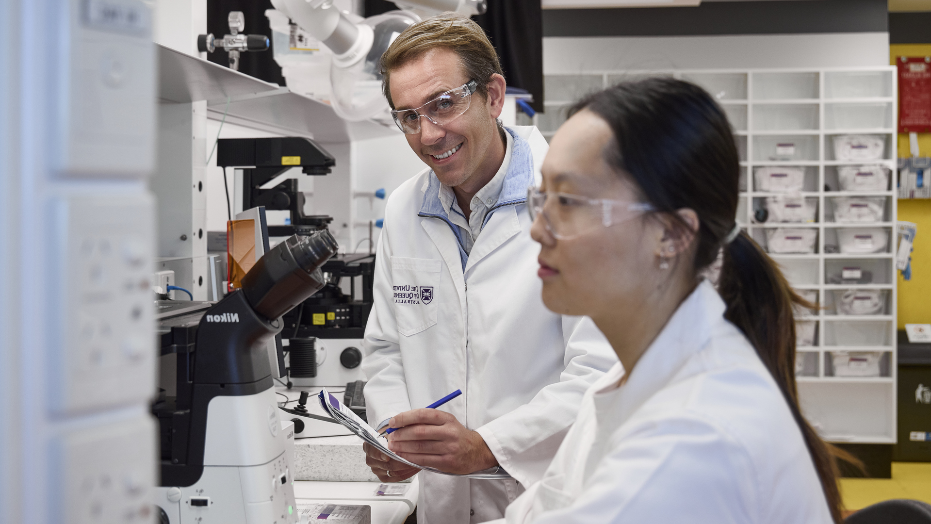 Two researchers in a laboratory work beside a microscope and other scientific equipment.