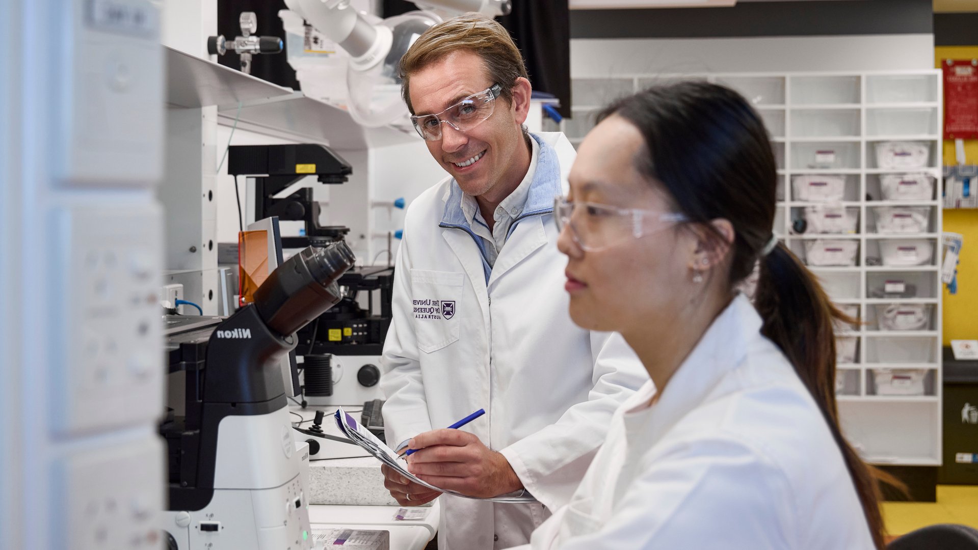 Two researchers in a laboratory work beside a microscope and other scientific equipment.