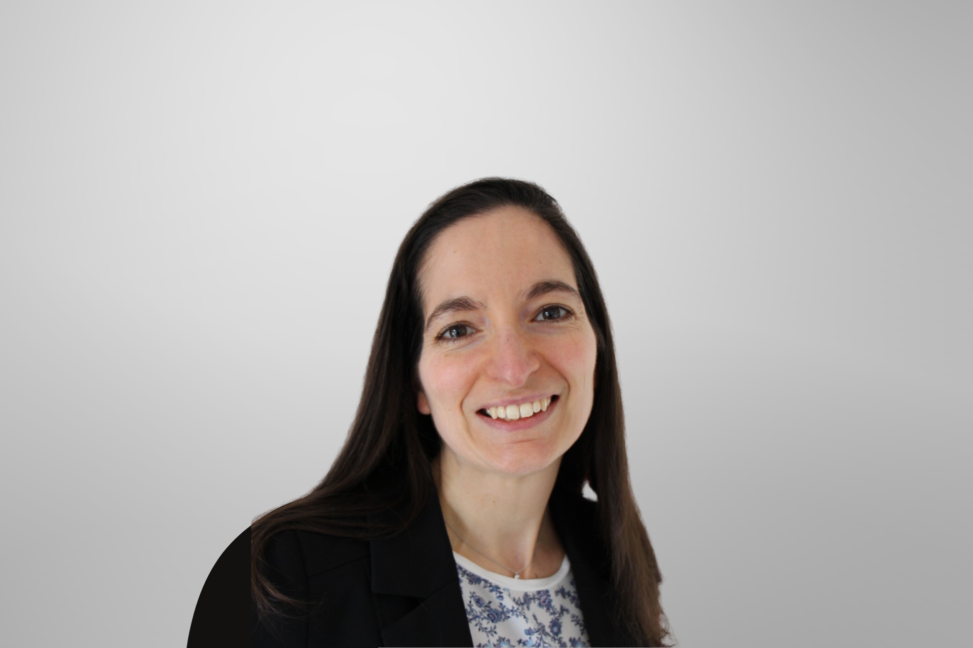 A professional woman wearing a blazer and a floral shirt, displaying a warm smile.