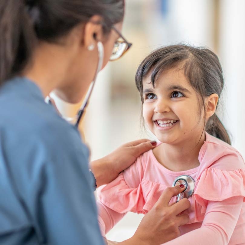 Young child in pink top smiling at doctor who has stethoscope on her chest