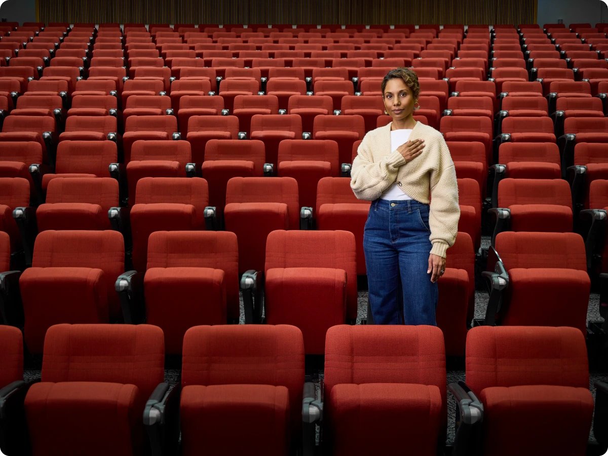 Dr Sonia Shah Standing in a empty lecture theater with her hand on heart 