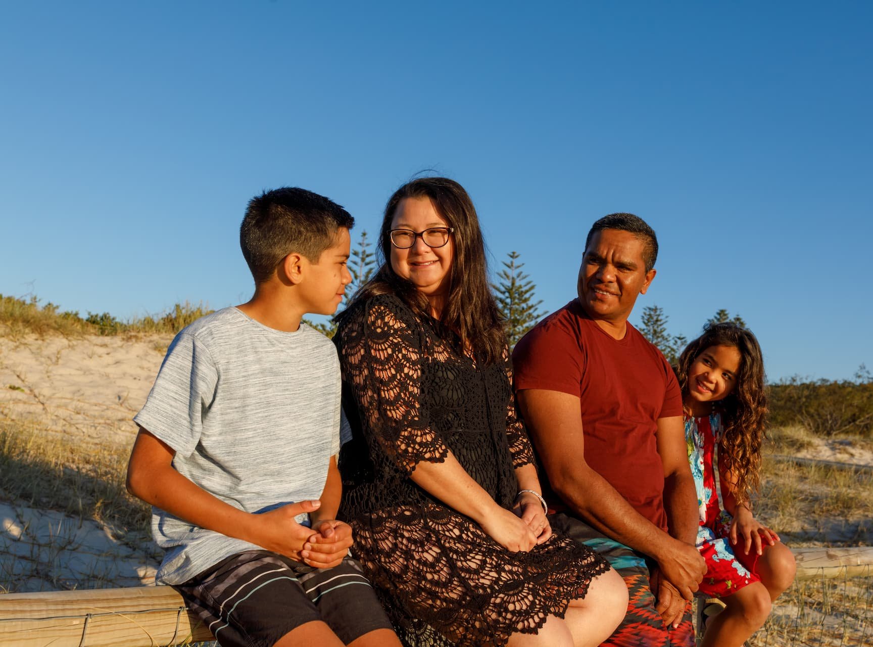 Family with mum, dad, boy and girl, sitting smiling at each other on the beach