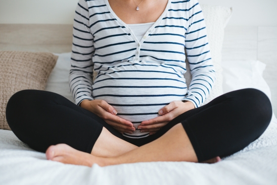 A pregnant woman gently cradling her belly while sitting on a bed.
