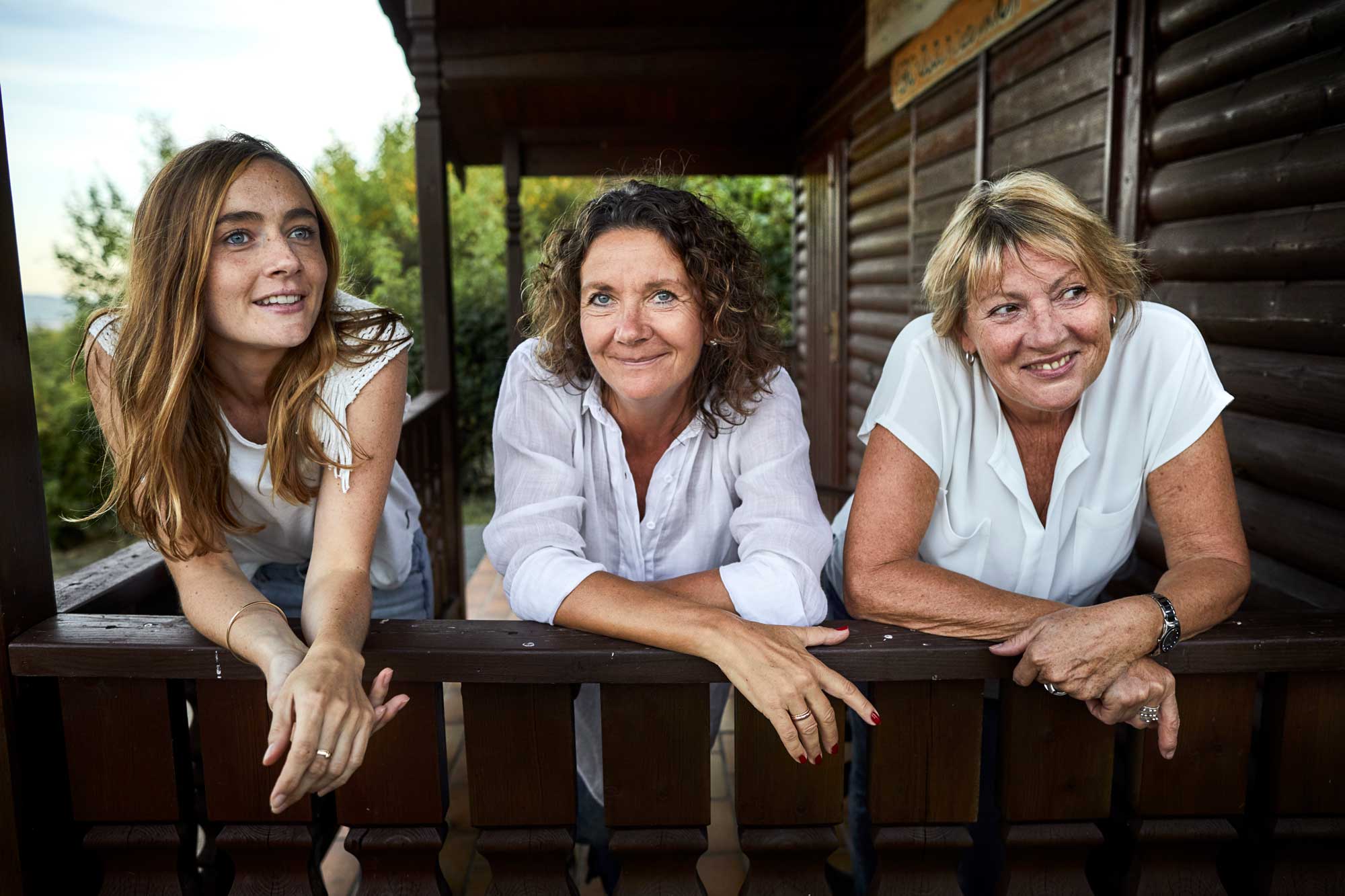 Three women standing on a balcony, wearing white shirts