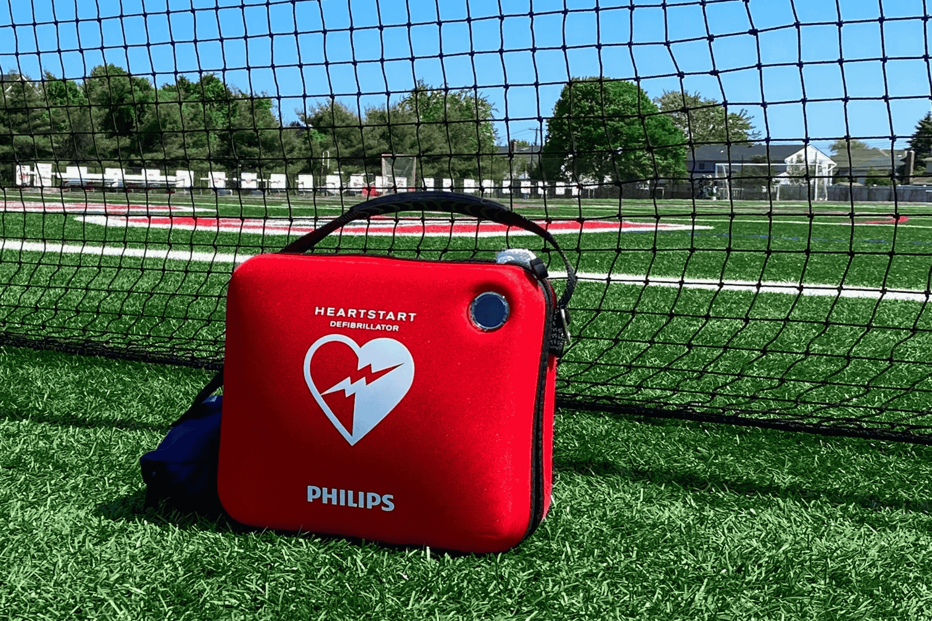 An AED resting in front of netting on a soccer field