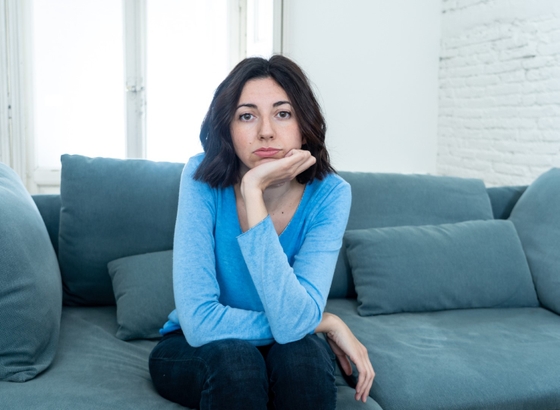 A woman sitting on a couch, deep in thought, with her chin gently resting on her hand.