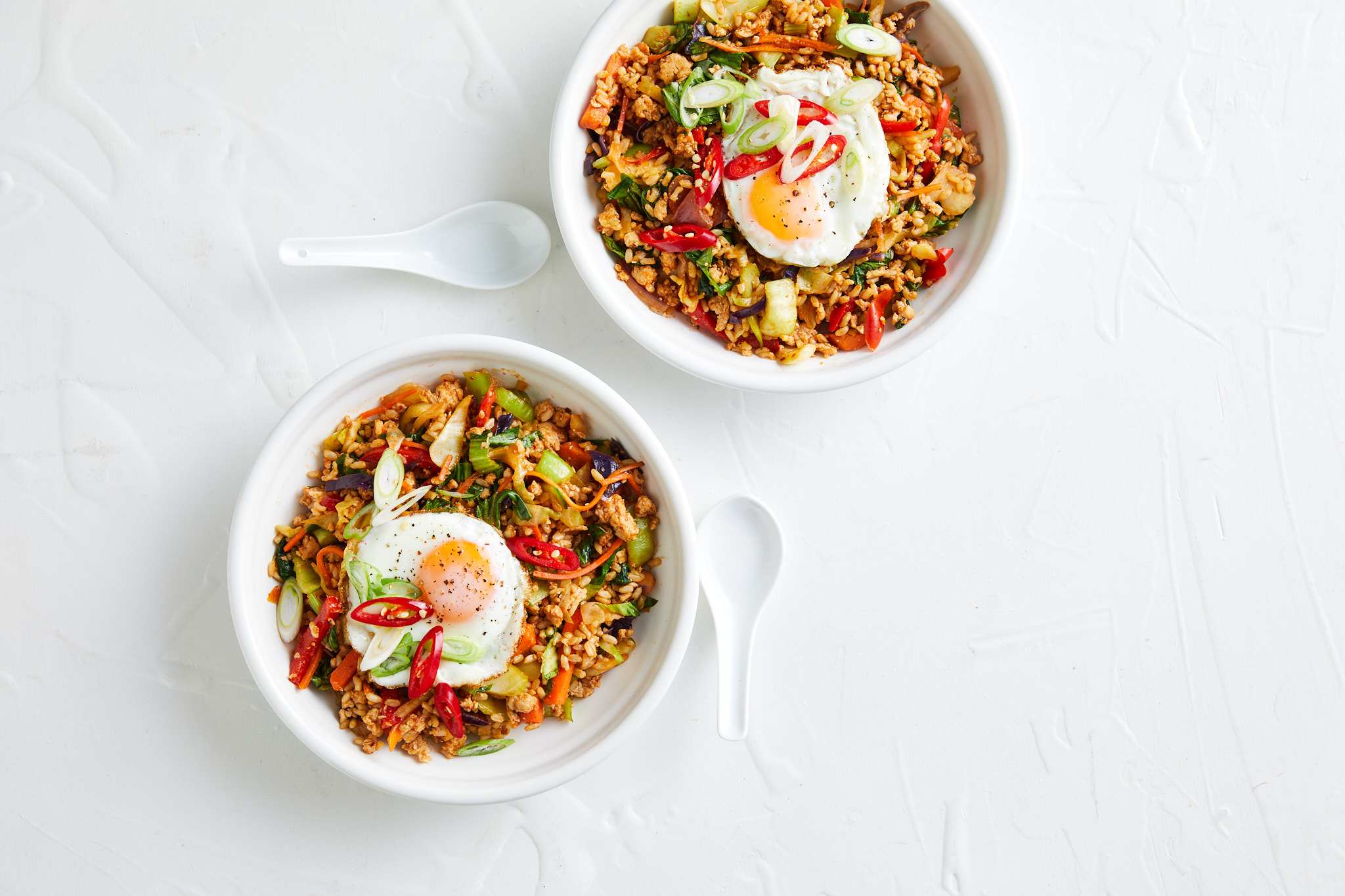 Two bowls of food topped with an egg, rice and vegetables