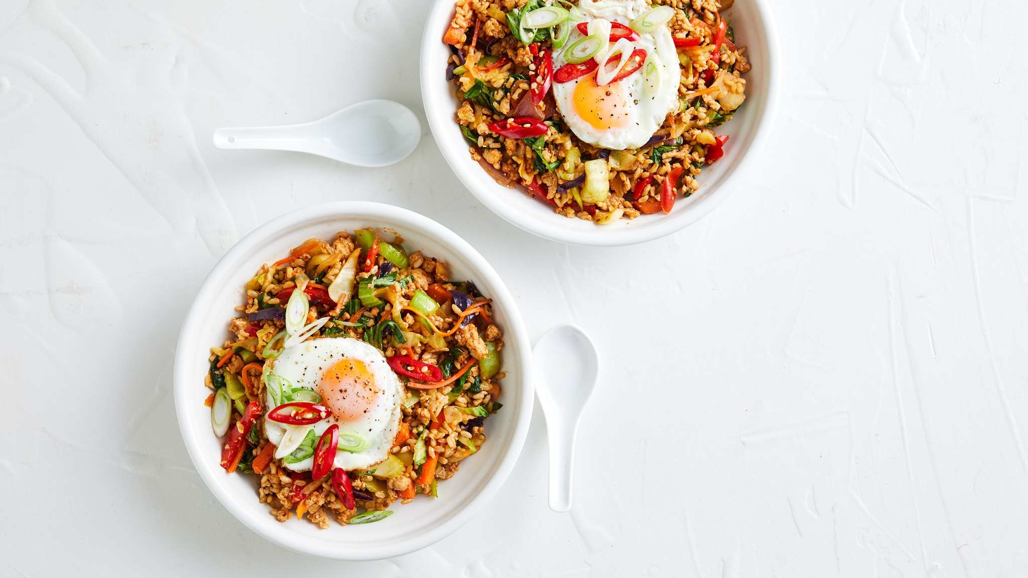 Two bowls of food topped with an egg, rice and vegetables