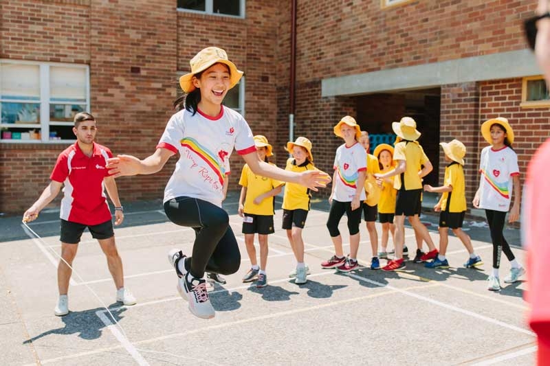 Group of school kids in bright colours doing Jump Rope for Heart in playground