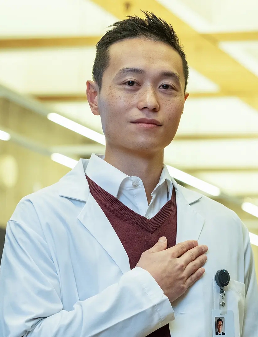 Dr Christopher Wong, standing in a white coat holding his heart on his heart