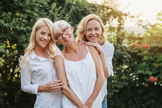 Three women standing together in a garden, smiling and enjoying each other's company.
