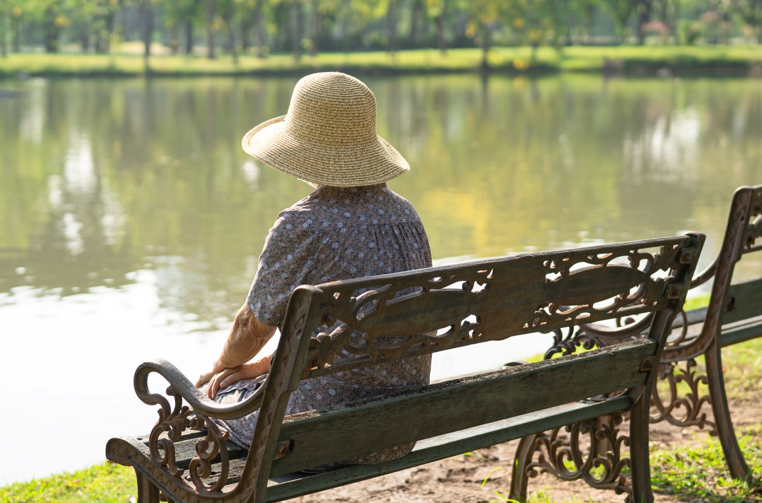 Person sitting alone on a park bench beside a lake.