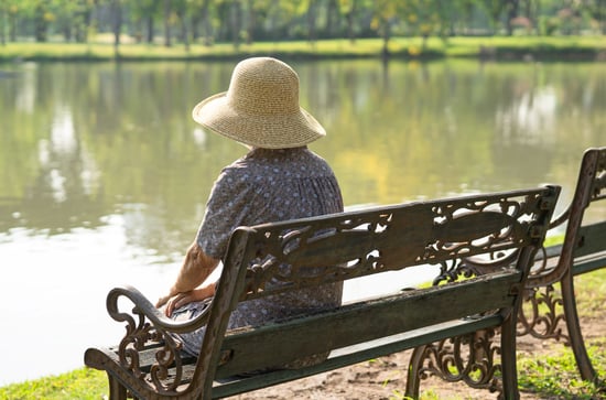 Person sitting alone on a park bench beside a lake.
