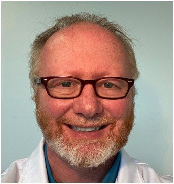 A bearded man with glasses smiling warmly.