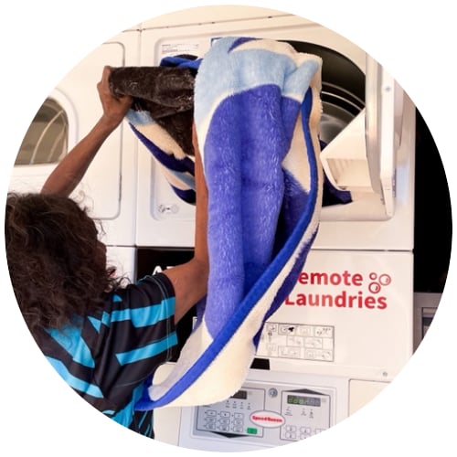 Person placing a large blue and white blanket into a commercial dryer at a remote laundry facility.