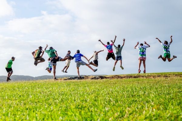 Young people in a line jumping in the air on a grass hill