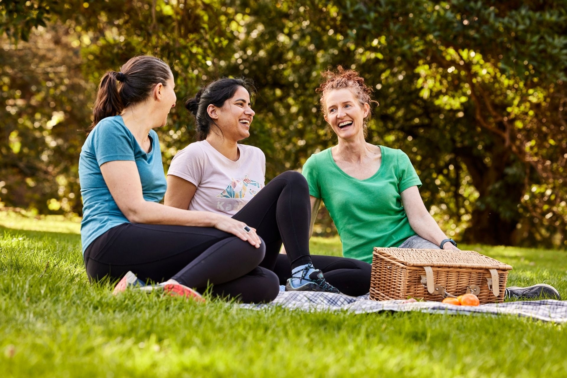 A group of woman sitting outdoors in a park, socialising over a picnic.