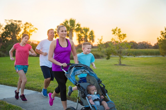 A family of four jogging together in a park, enjoying a healthy and active lifestyle amidst greenery and fresh air.