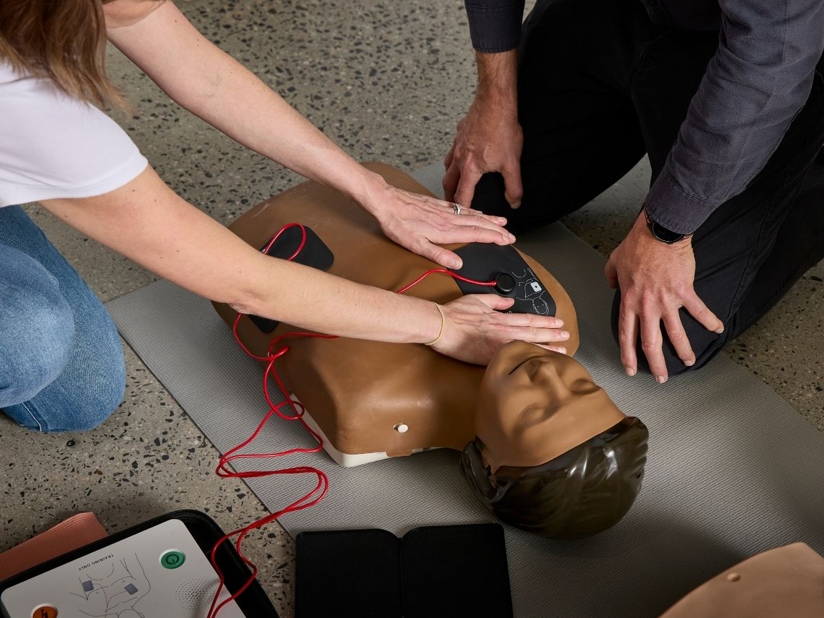 A trainer showing someone how to apply AED pads to a mannequin's chest