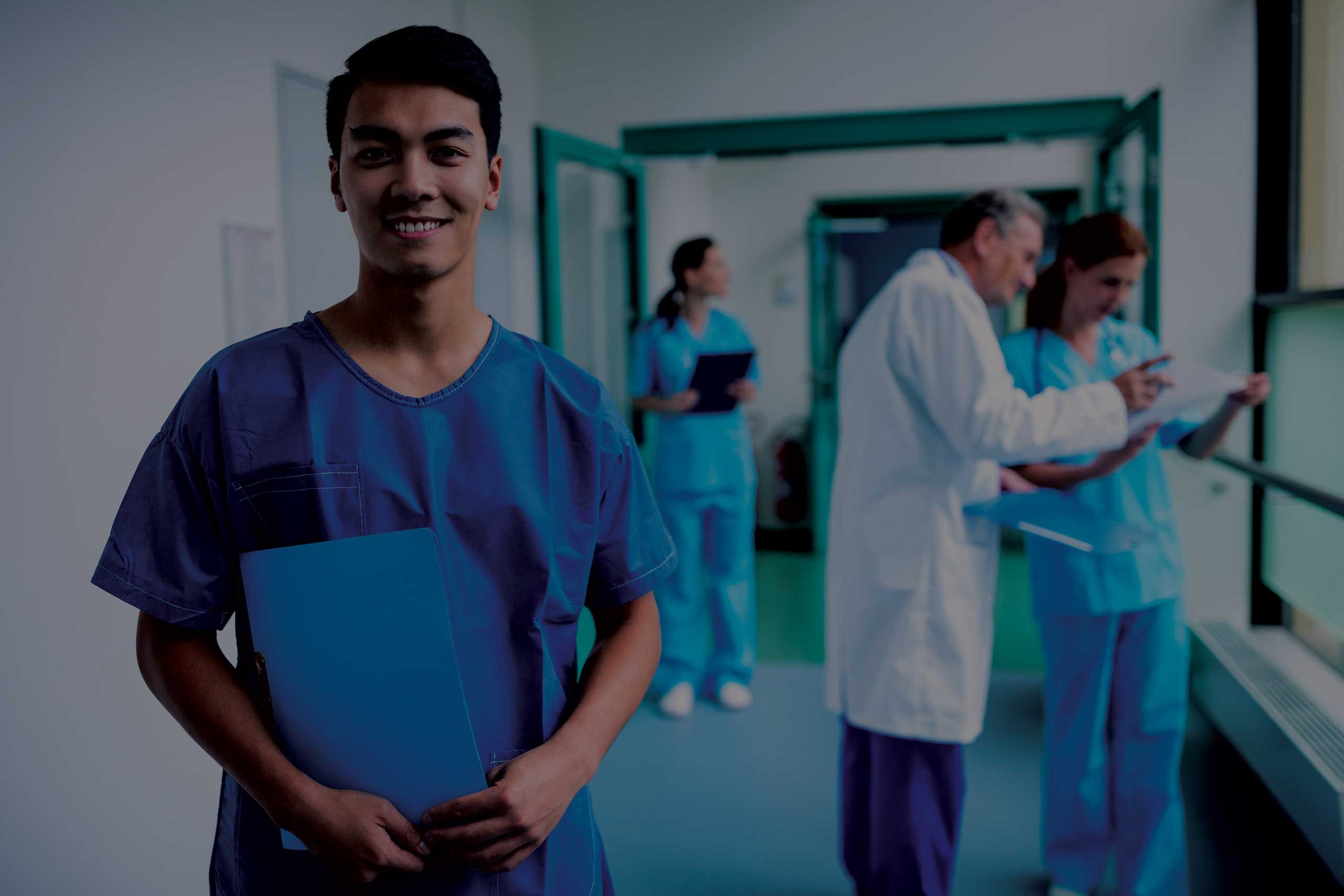 Healthcare professional in scrubs standing in a hospital corridor with medical staff in the background