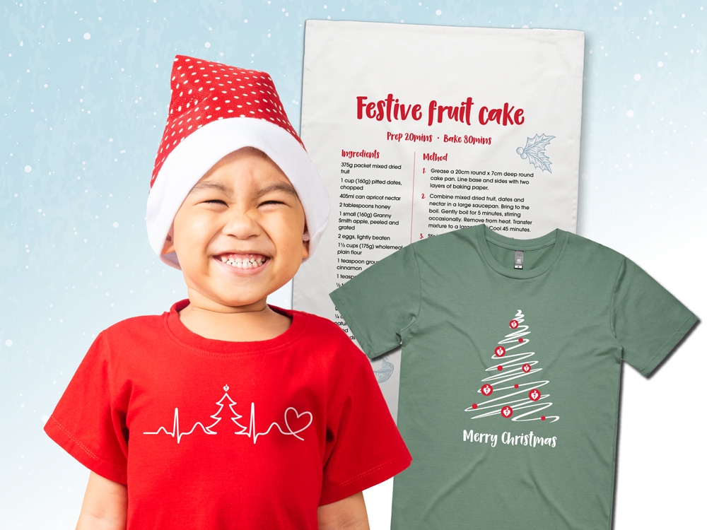 A young child smiling in a Christmas hat, standing in front of a festive tea towel and t-shirt