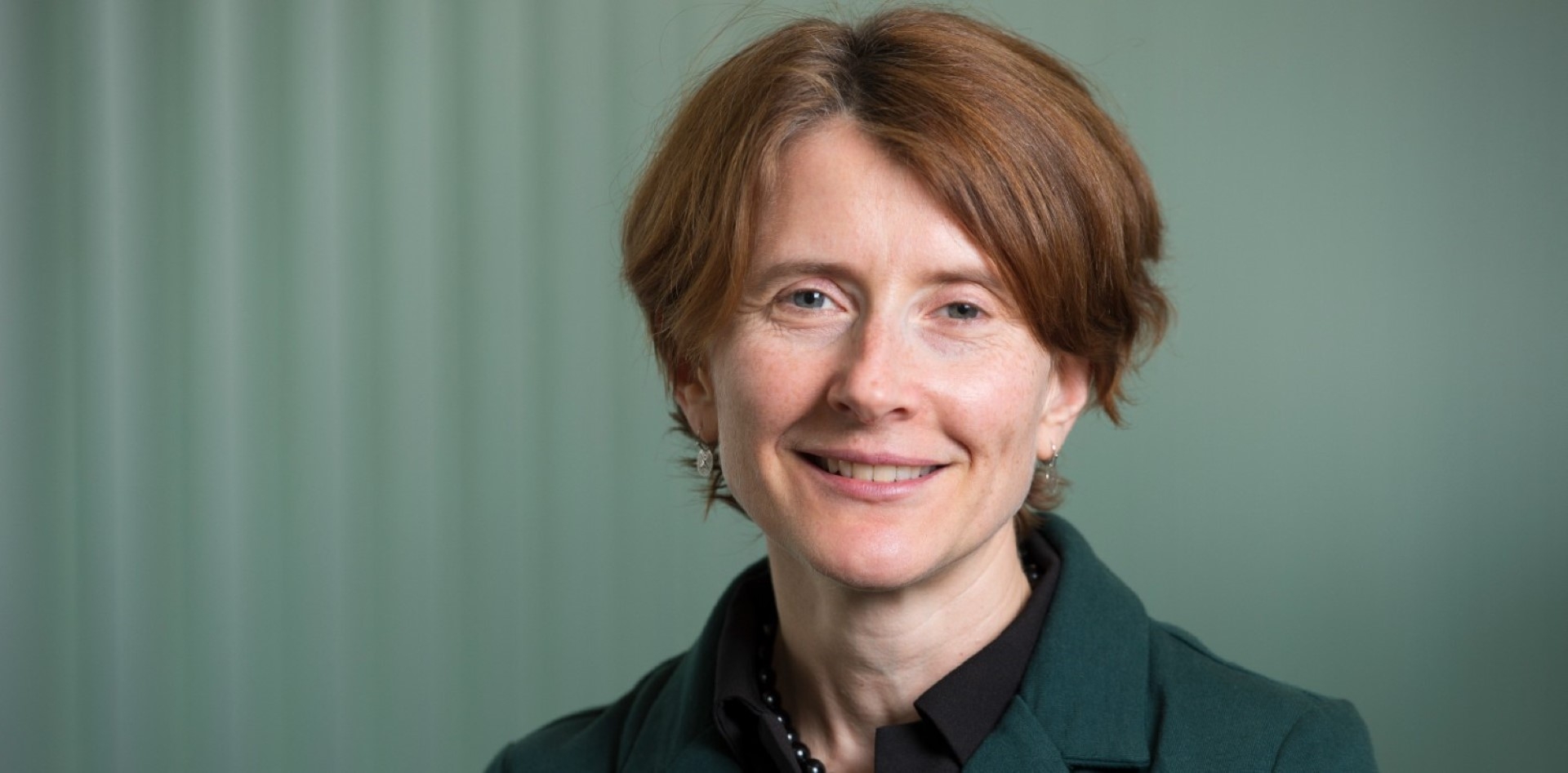 Associate Professor Lisa Moran smiling at the camera in front of a teal coloured background