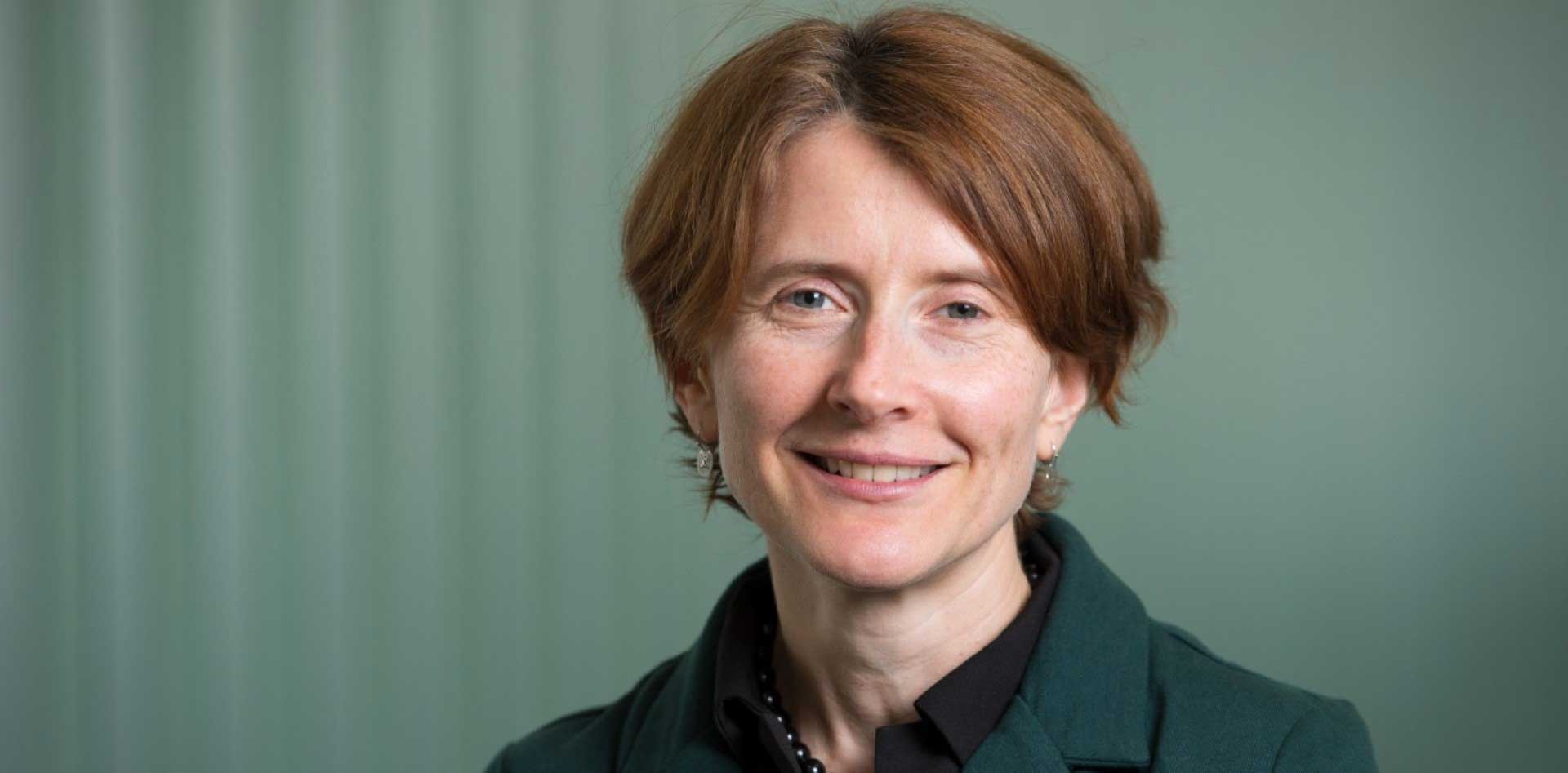 Associate Professor Lisa Moran smiling at the camera in front of a teal coloured background