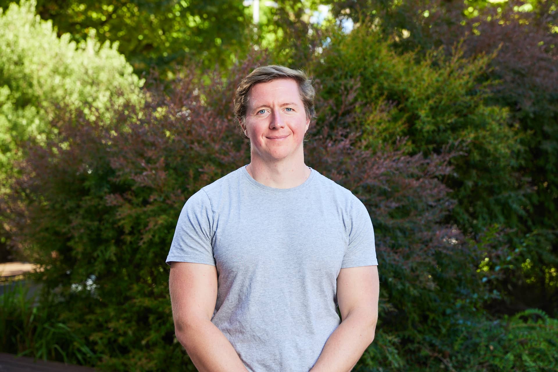 Dr Jedidiah Morton standing and smiling in a grey shirt