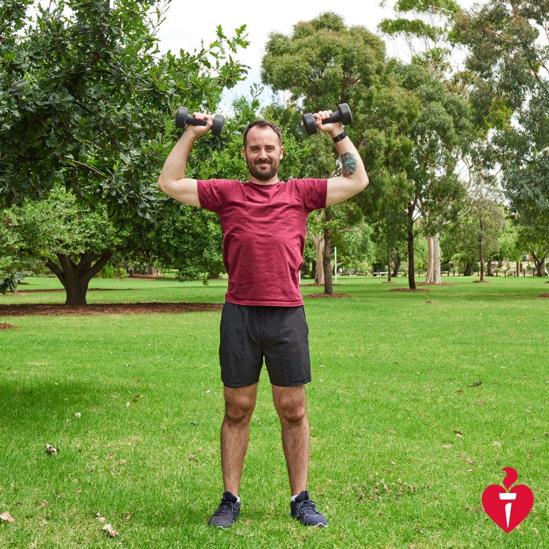 Man dressed in maroon tshirt doing shoulder presses with 2kg weights