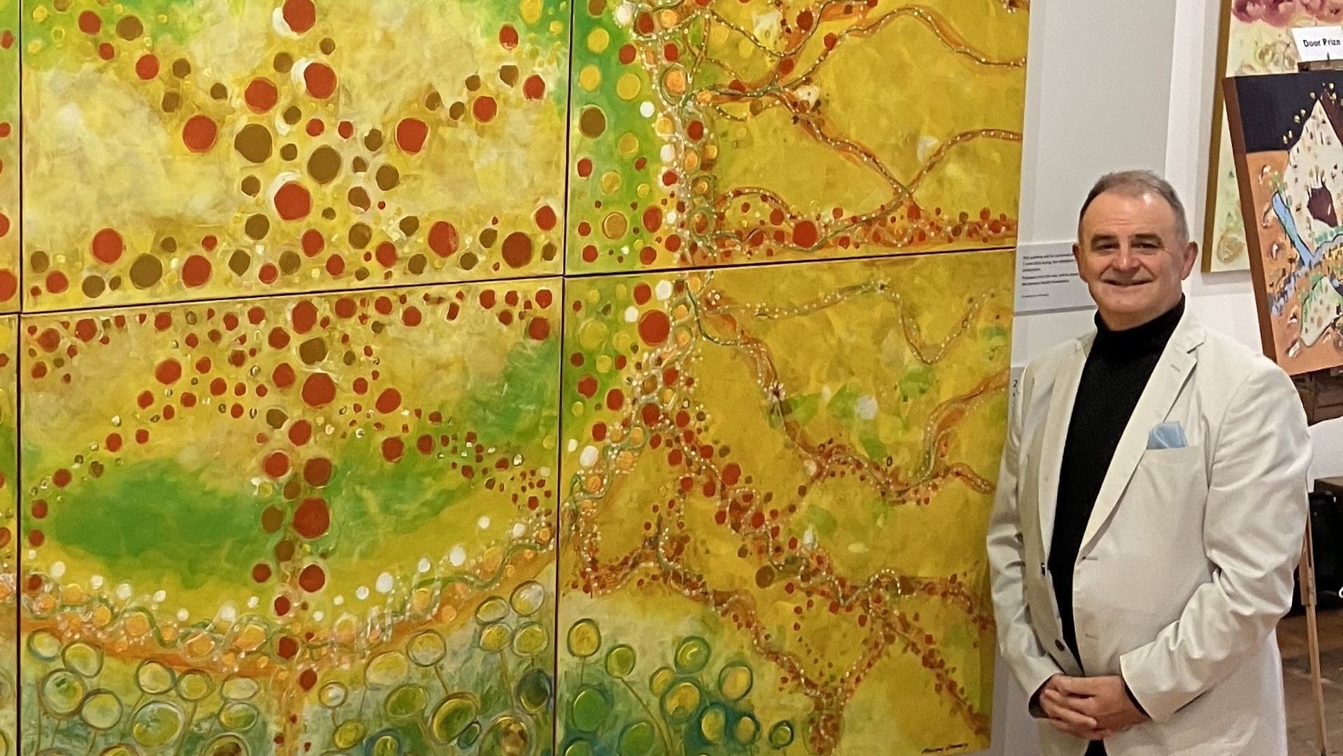 Murray Cheney, a heart surgery survivor, stands in front of his artwork at an exhibition.