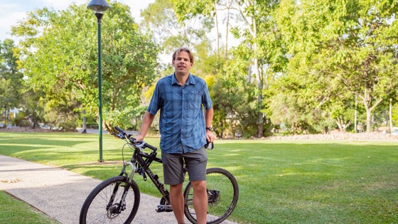 Professor Corneel Vandelanotte standing next to his bike with a background of grass and trees