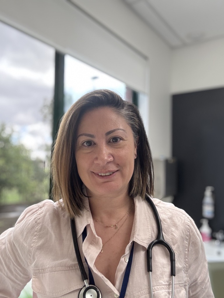 Smiling nurse wearing a stethoscope, standing indoors.