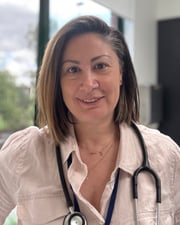 Smiling nurse wearing a stethoscope, standing indoors.
