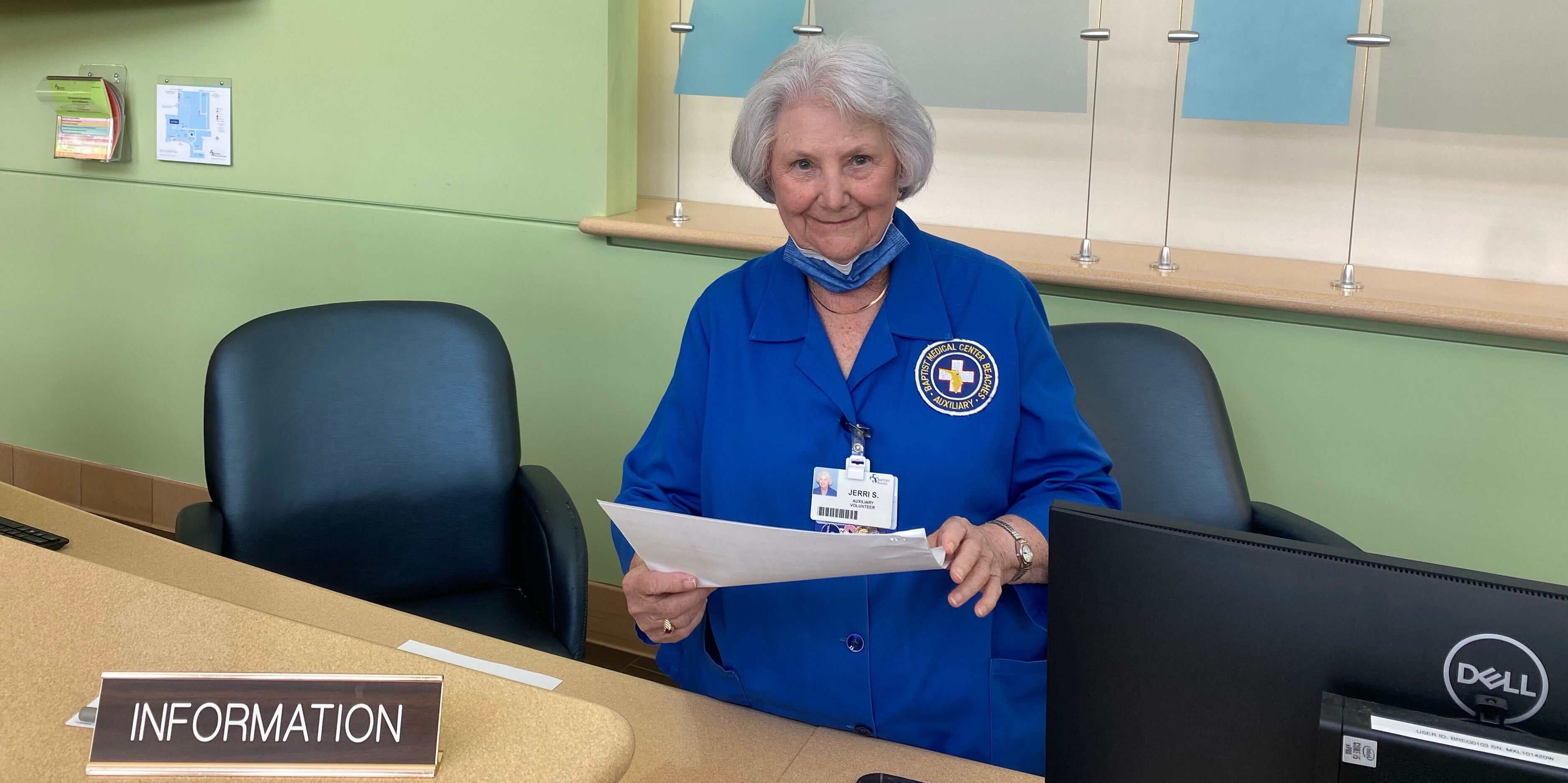 91 year old woman, Jerri Snavley, sitting behind an information desk at a hospital and smiling