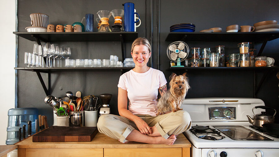 Lady and her small dog sitting cross-legged on a kitchen counter in a neatly organised kitchen.