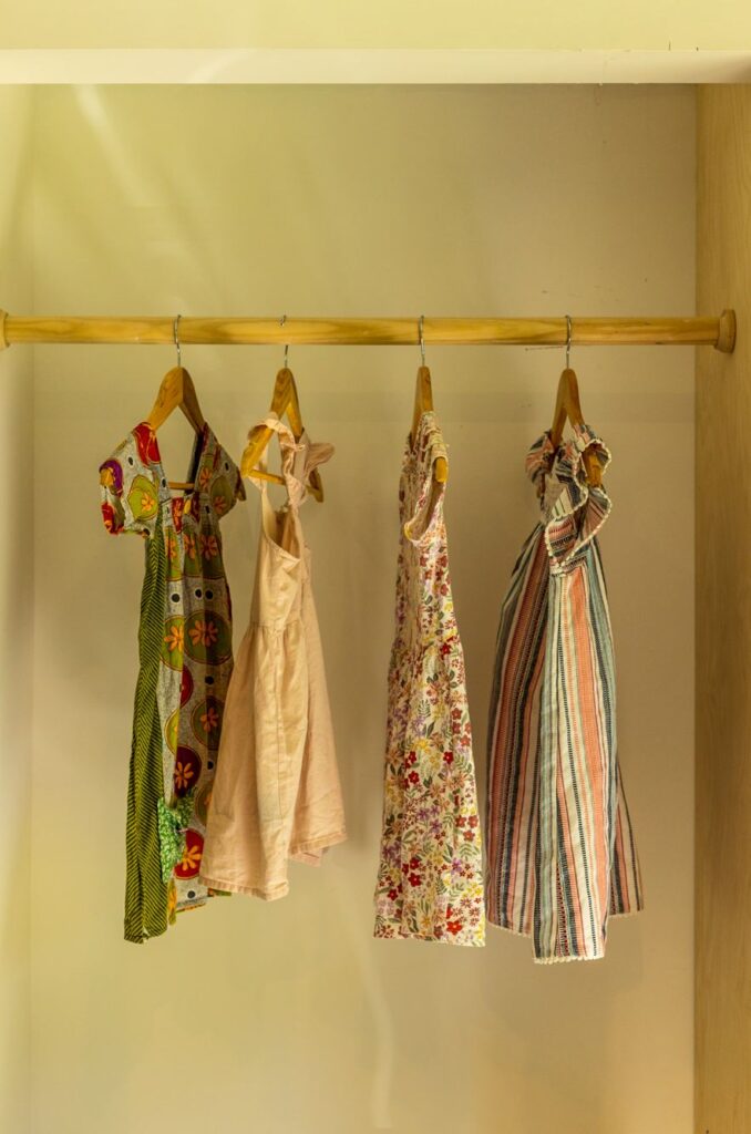 Four dresses hanging on a wooden pole in a wardrobe.