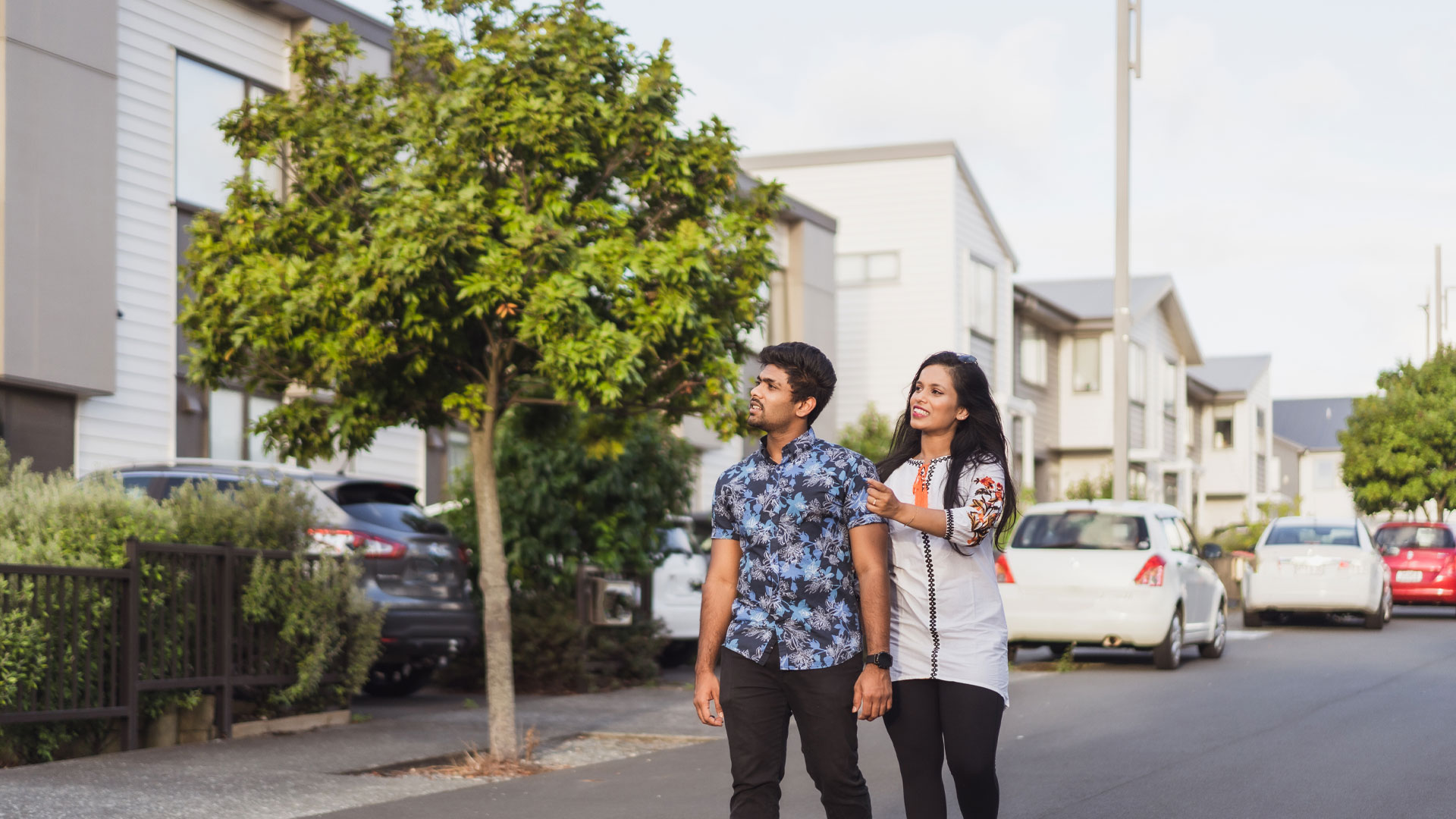 Young couple of first home buyers, looking to buy their first home in NZ, walking down a street of new builds.