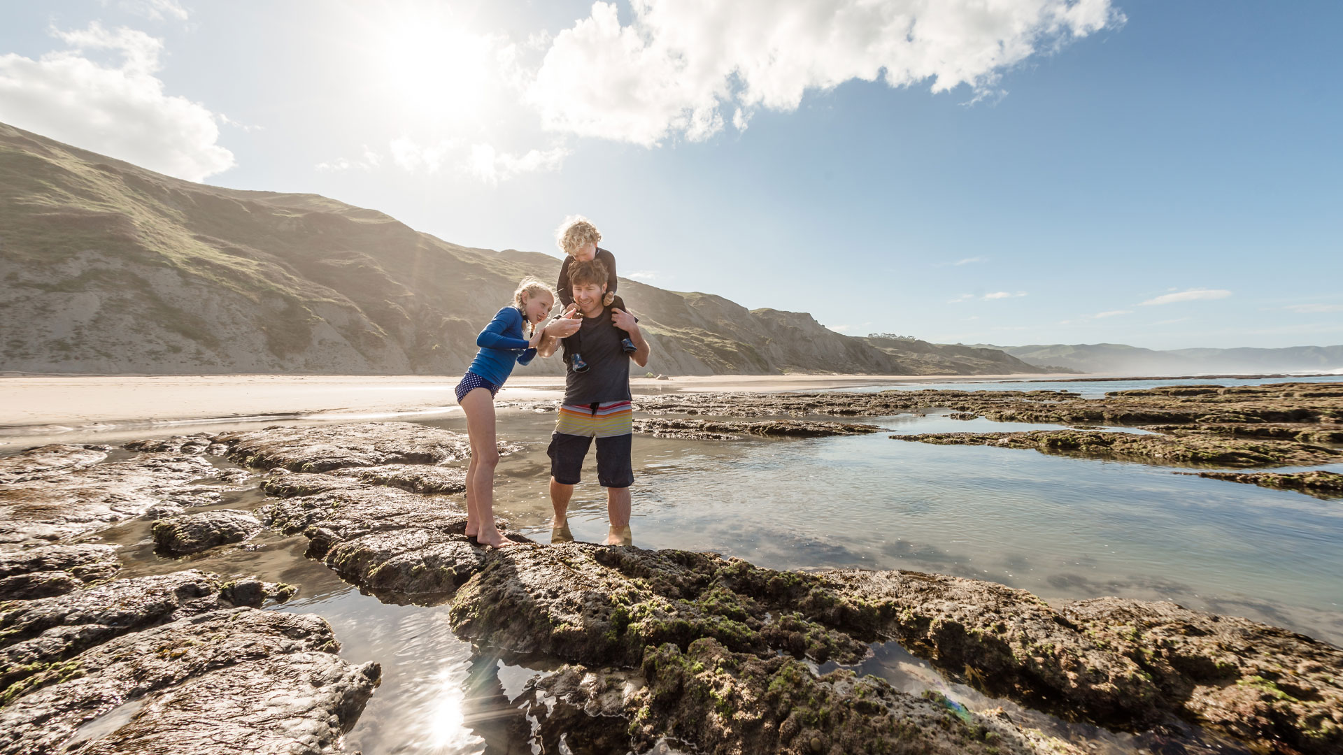 Family walking on a beach in the Hawke's Bay looking in rock pools.