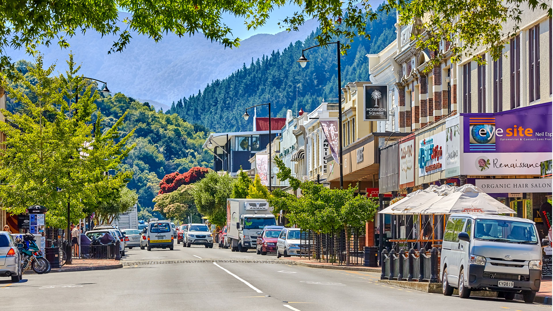 A street view in Nelson, showing shops, with tree-covered hills in the background.