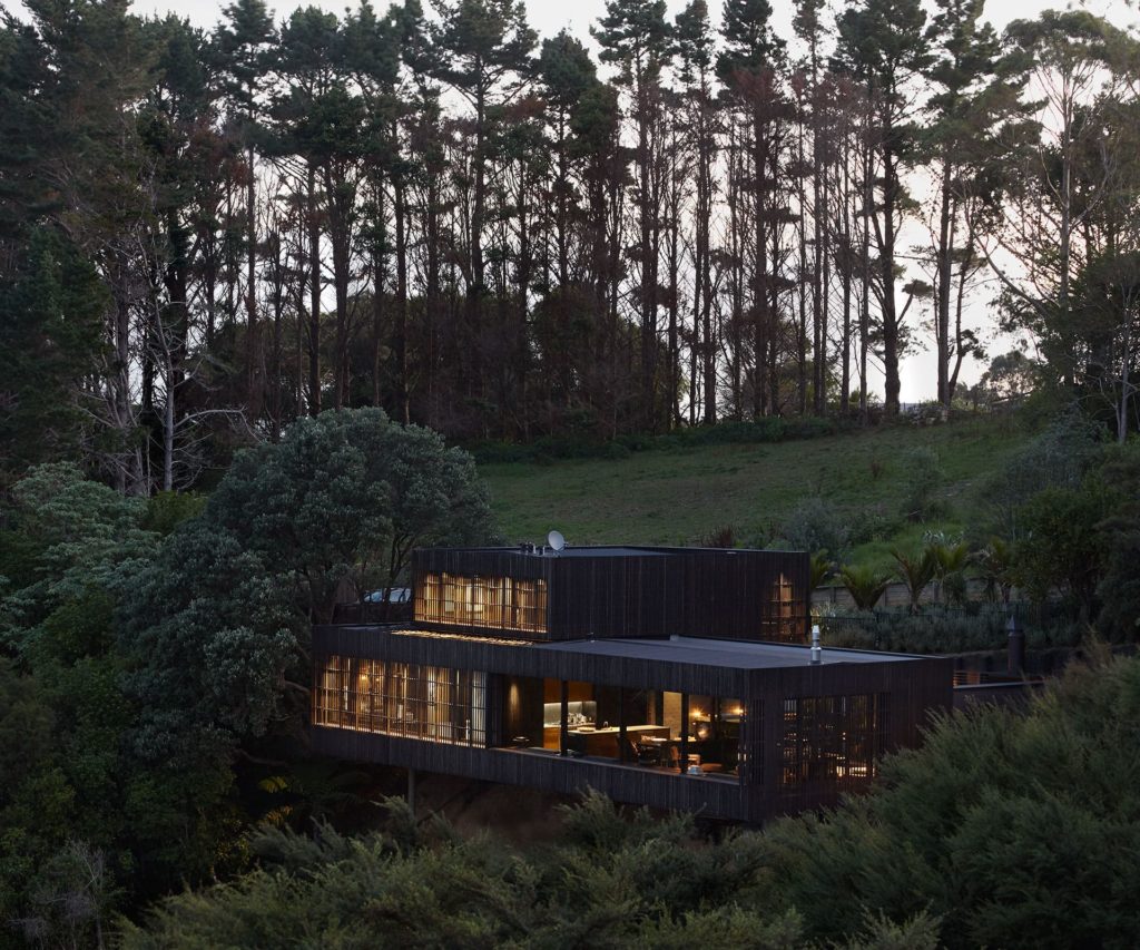 A modern home tucked into a hill with large trees above.