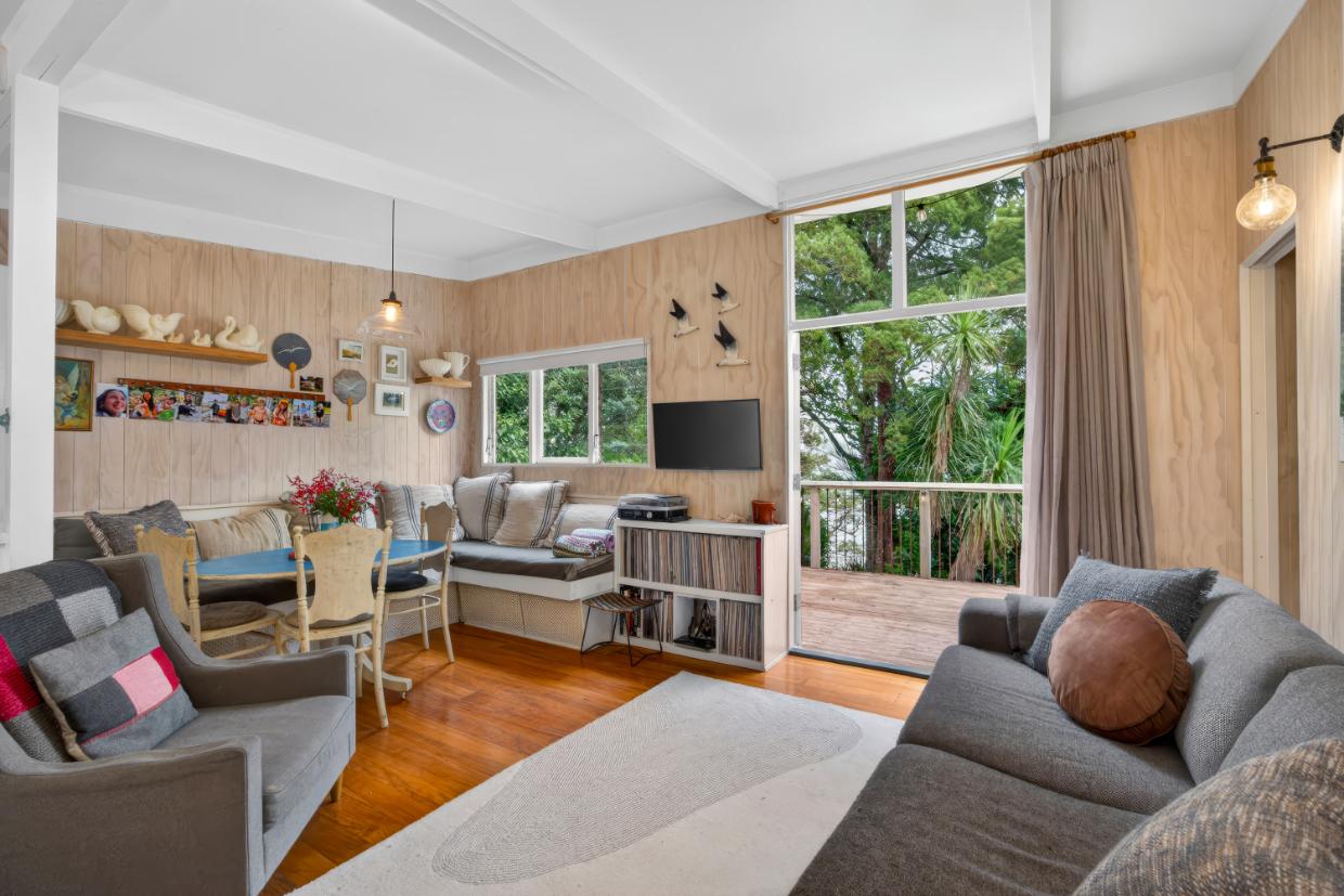 The bach opens out to a deck, front and back, with a sea view through trees. The original partitions between rooms were replaced with proper walls and doors, and the bach was fully insulated. Photo: Ray White