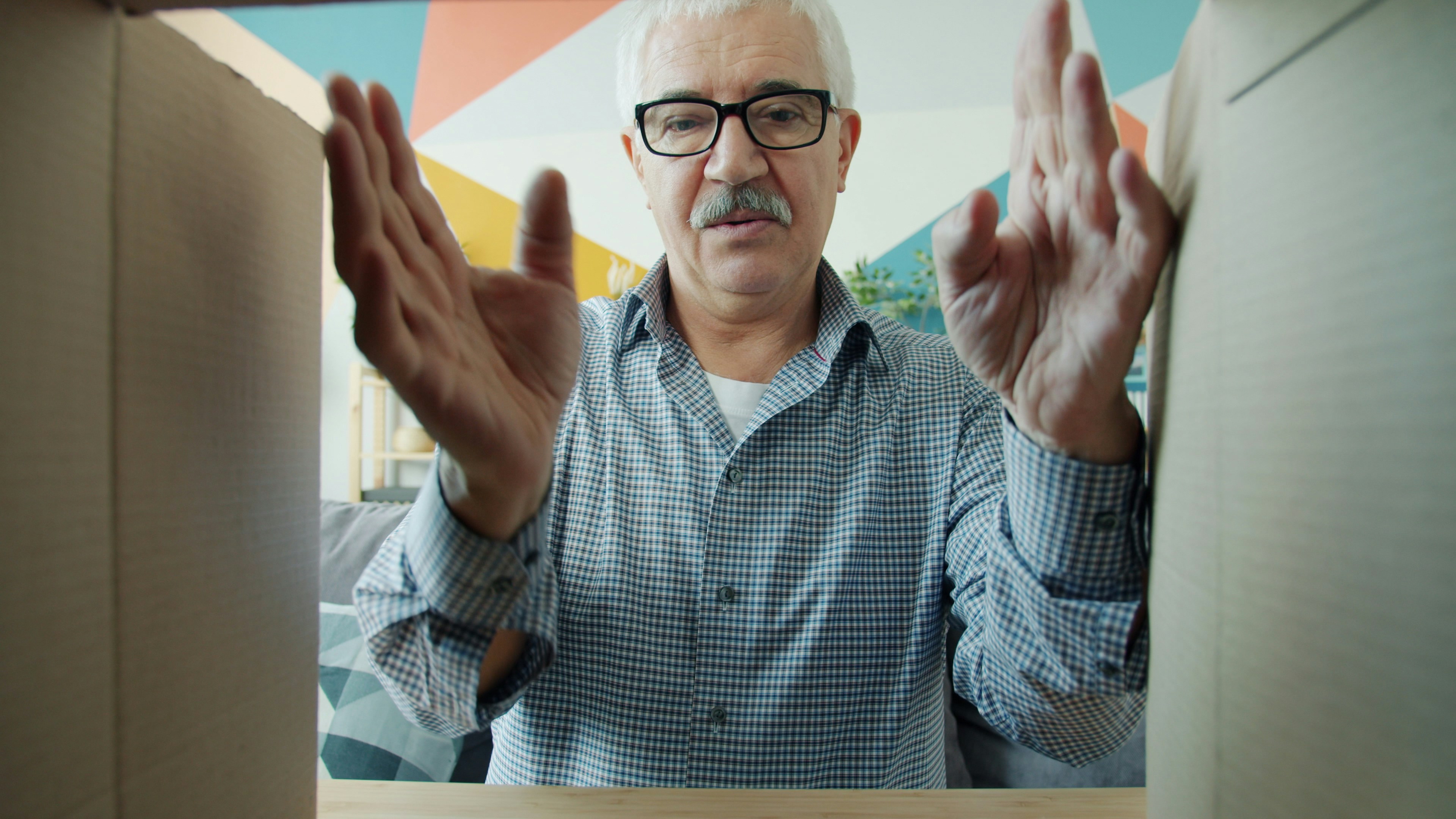 An elderly man is reaching into a cardboard box. The perspective is from inside the box, looking up at the man.