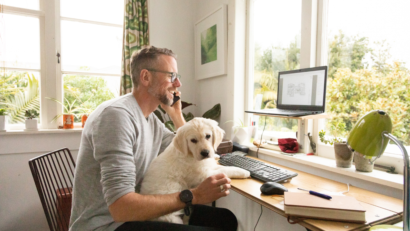 Man talking on phone in office dog in lap. 