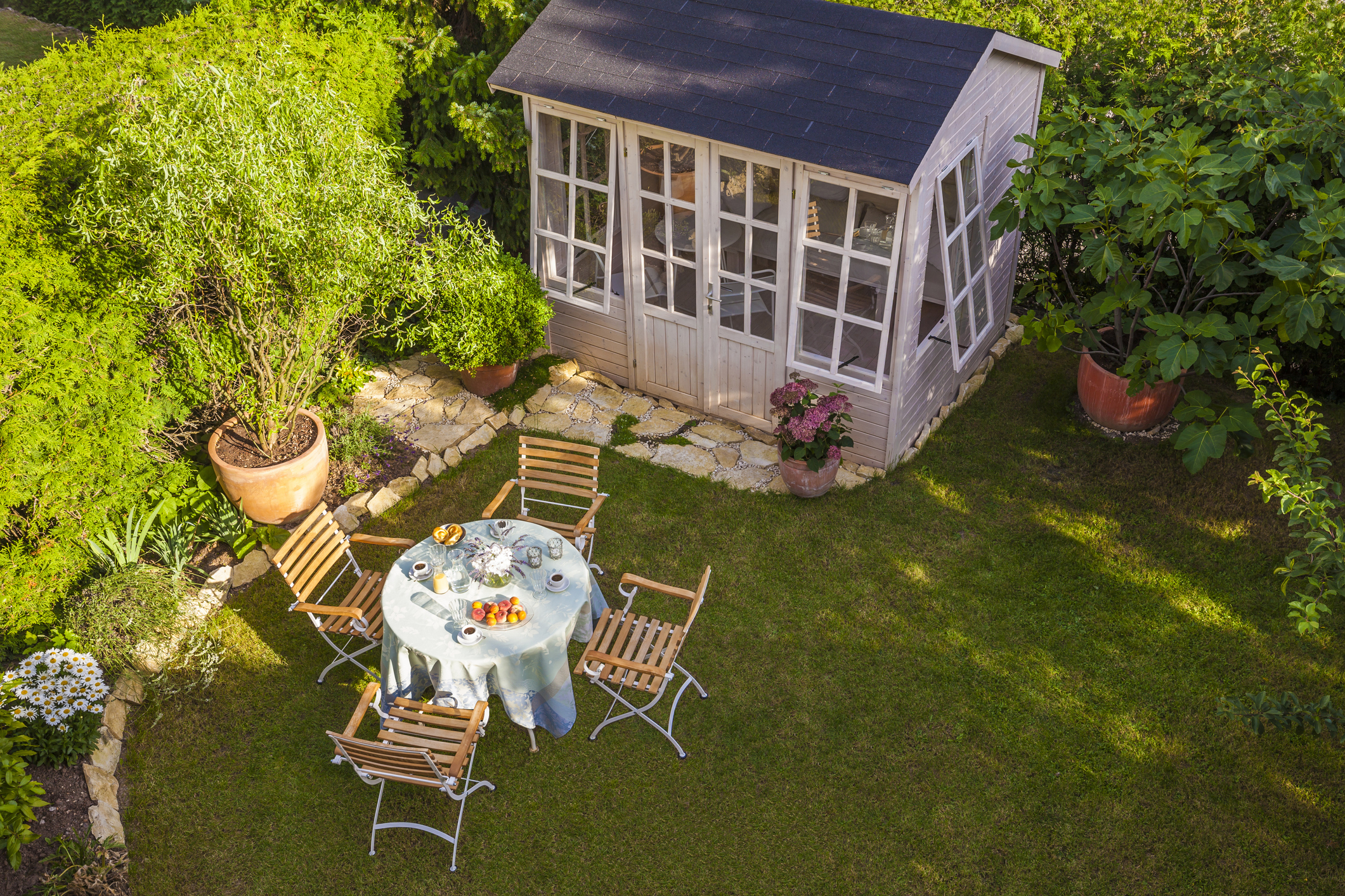 A rustic timber garden shed with a window and a shingle roof, surrounded by green trees and plants in a New Zealand backyard.