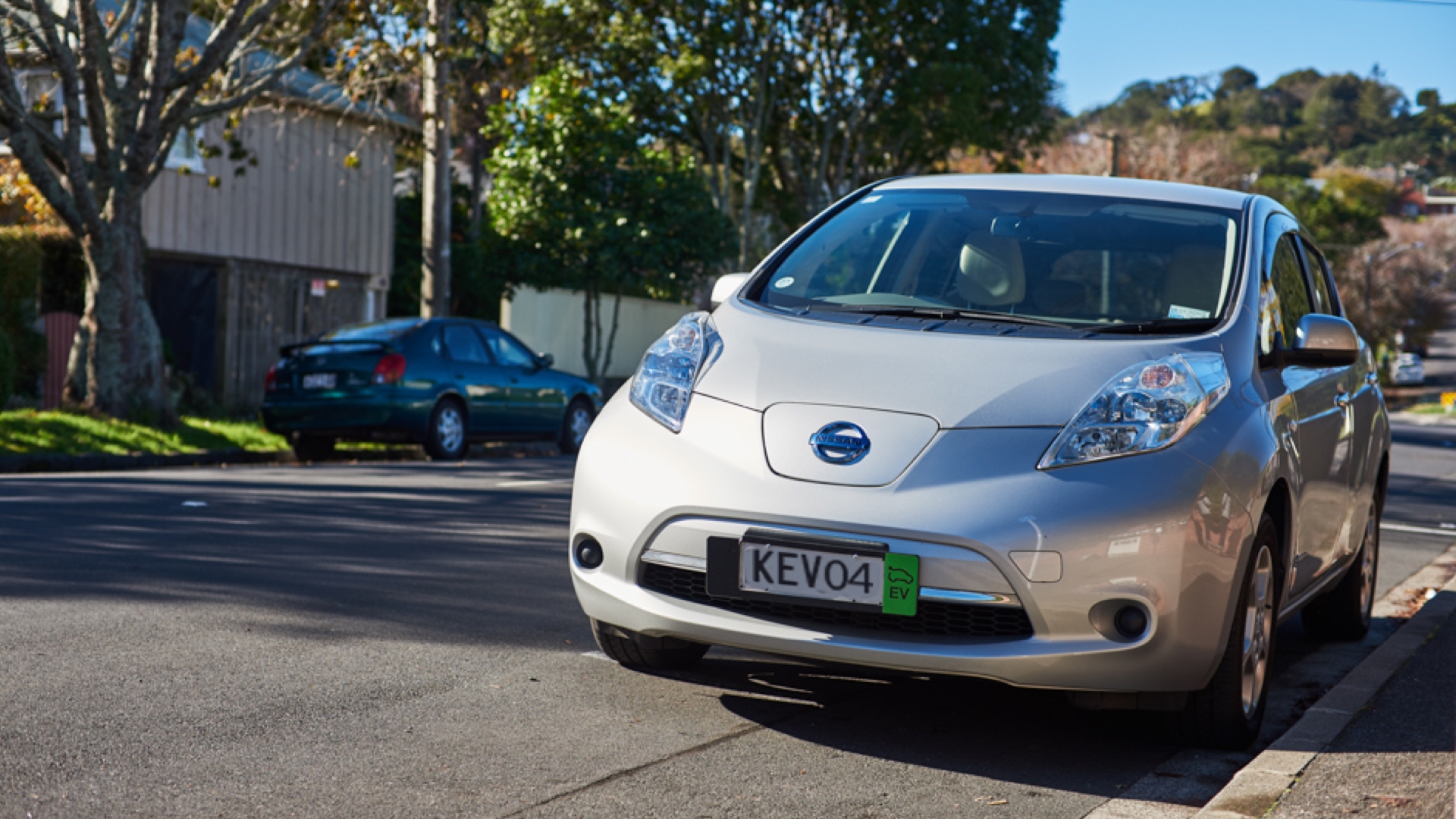 Front-on shot of a silver Nissan Leaf, parallel parked on a suburban street