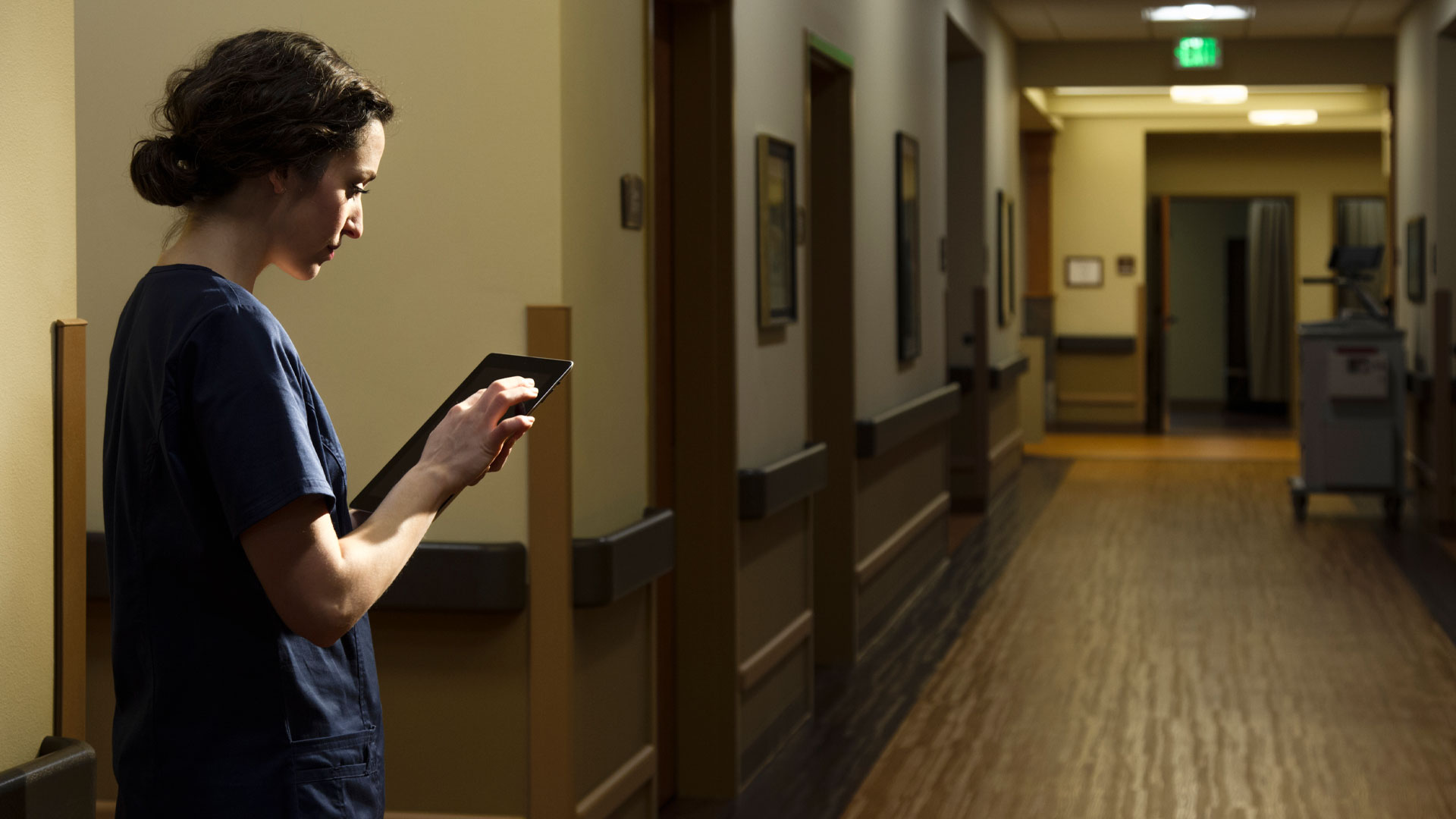 Nurse in scrubs working a night shift holding a tablet in the halls of a hospital.