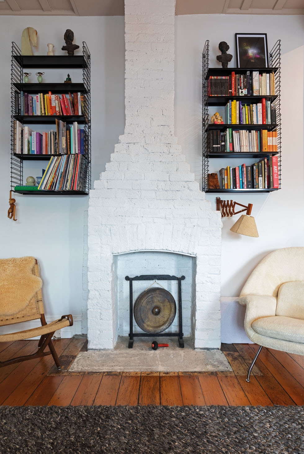 An unused fireplace nestled between two chairs and a pair of full bookshelves